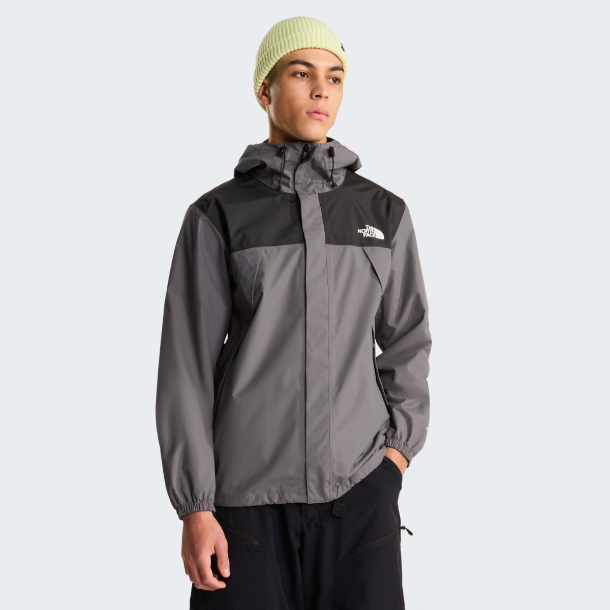 Male model wearing The North Face Antora waterproof jacket in smoked pearl gray with black chest panel and hood.