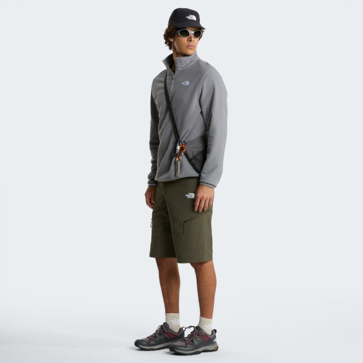 Full body side view of a model wearing The North Face Glacier fleece in mid grey heather with cap.