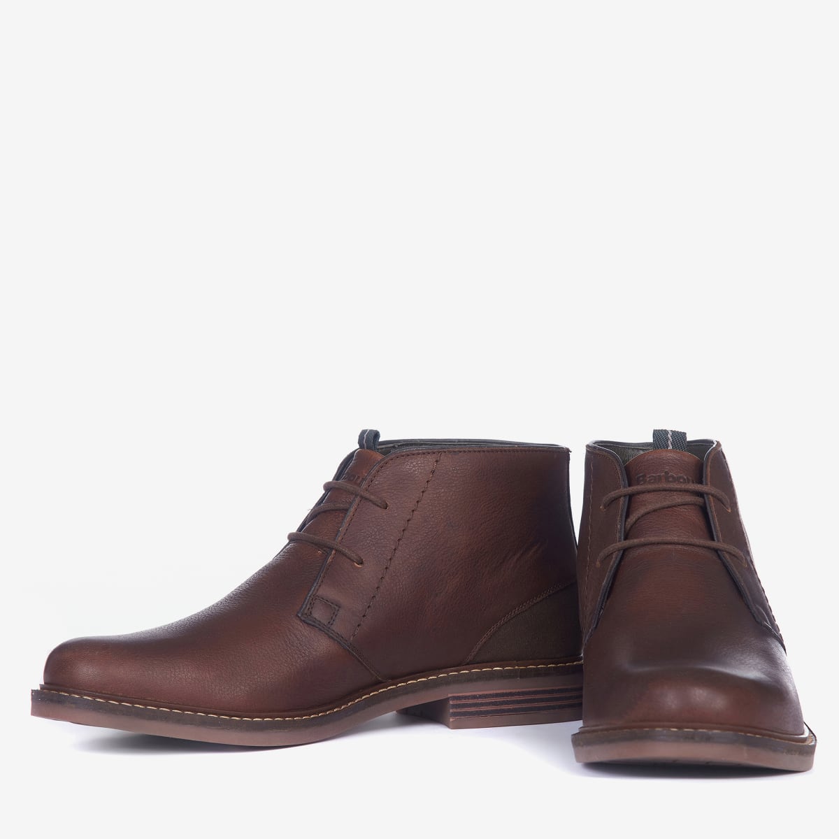 A pair of Barbour Readhead Men's Chukka Boots in teak color, featuring a lace-up closure, with tartan detail on the tongue and a metal Barbour badge.