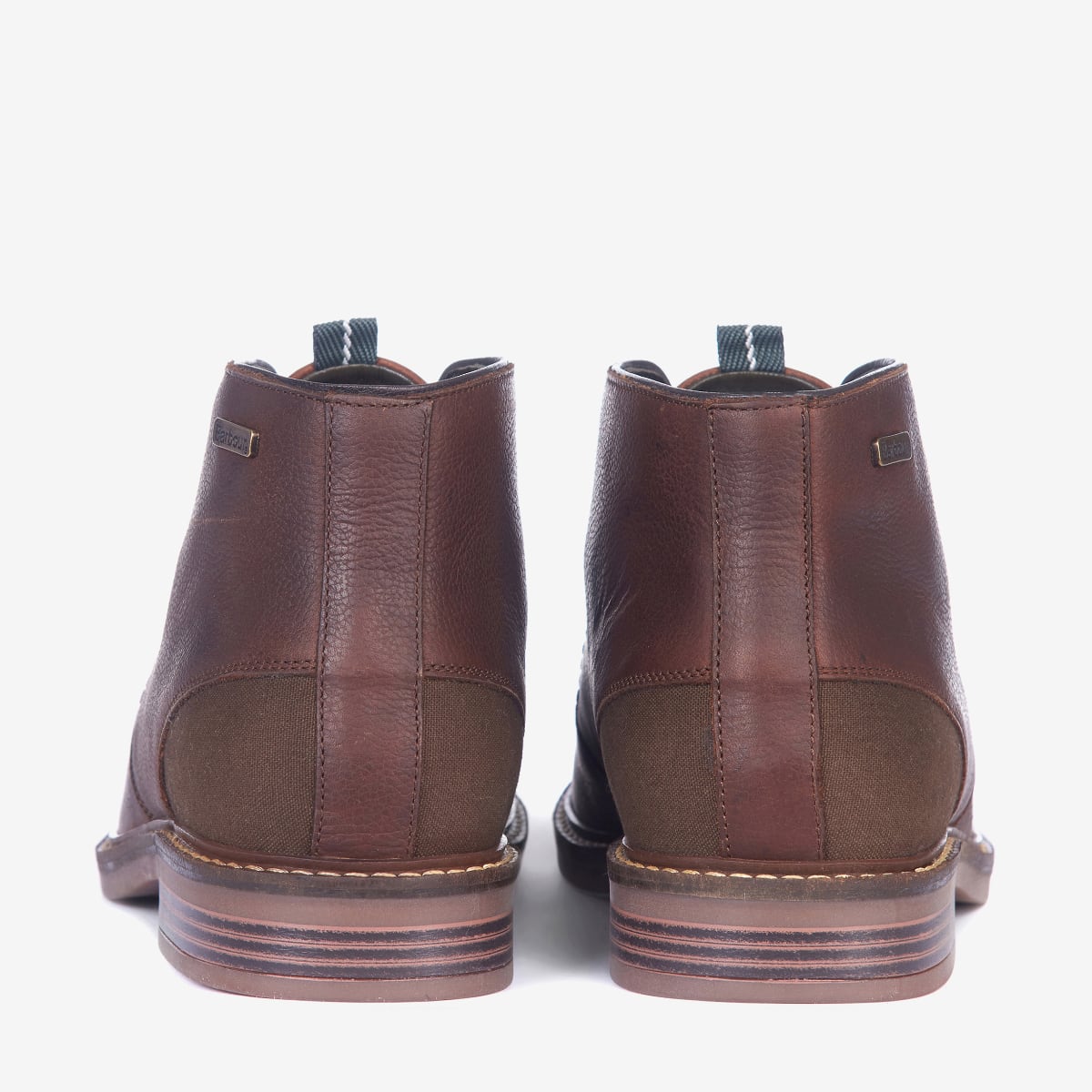 Rear view of a pair of Barbour Readhead Men's Chukka Boots in teak color, featuring a lace-up closure, with tartan detail on the tongue and a metal Barbour badge.