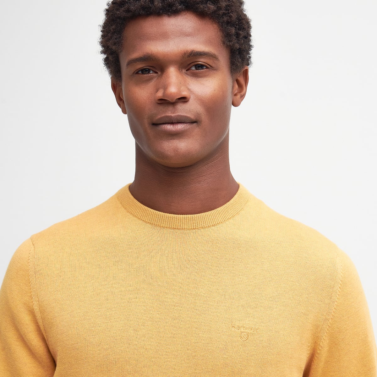 Close up of honey gold Barbour Pima Cotton Crew Neck jumper on a model showing knit texture and chest logo