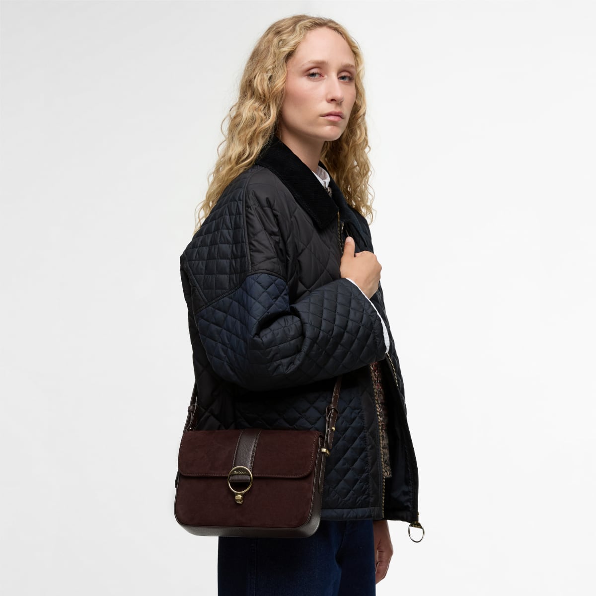 Model wearing Barbour Rosa crossbody bag over a dark quilted jacket.