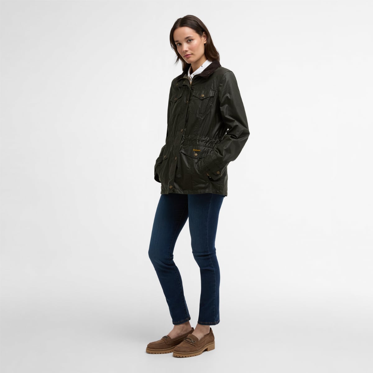 Woman wearing olive Barbour Summer Sapper waxed jacket with blue jeans and tan loafers