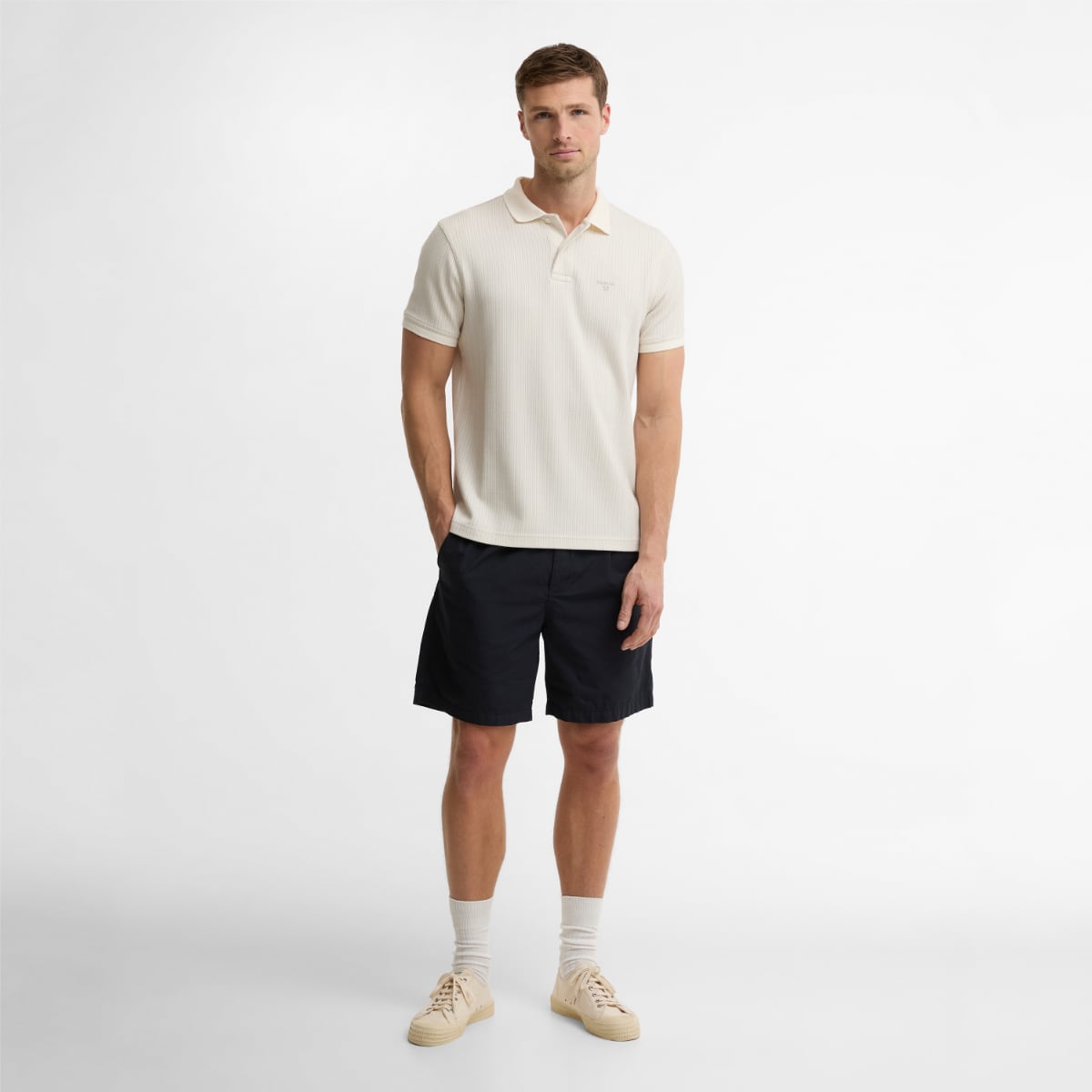Model wearing Barbour Harworth tailored men's polo shirt in whisper white with navy shorts.