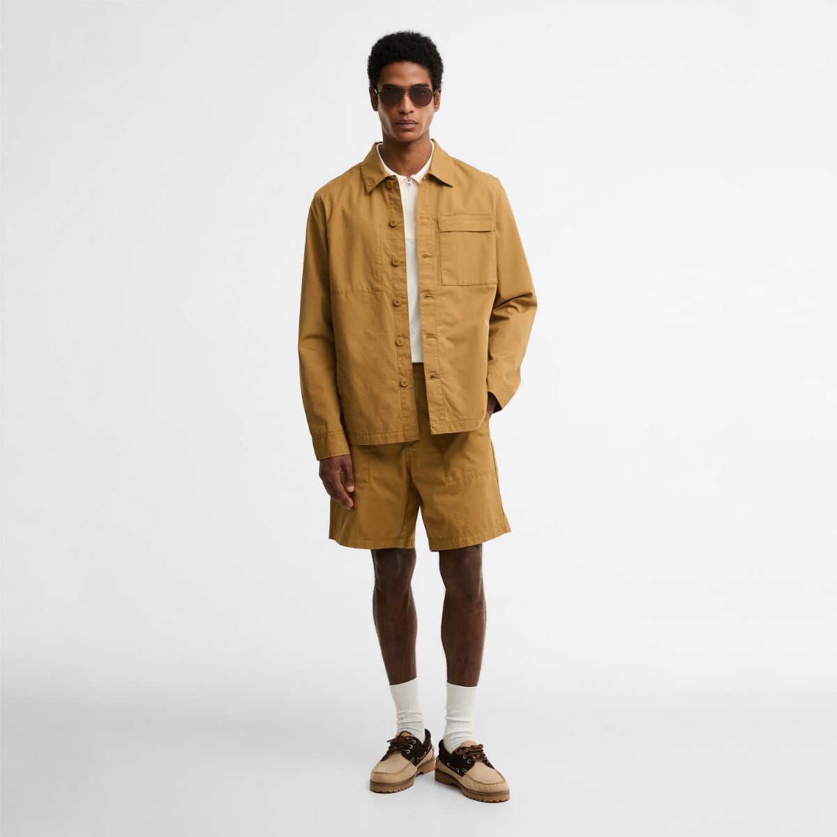 Male model wearing camel Barbour Sherburn overshirt with matching shorts and sunglasses.