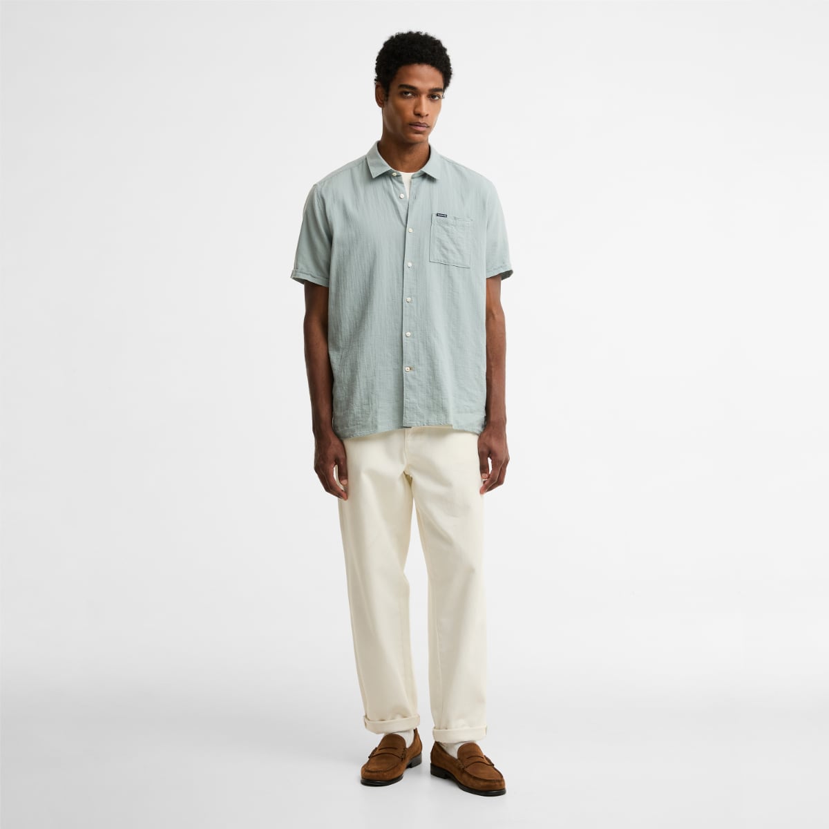 Barbour Kingswood short sleeve relaxed fit shirt in dusty slate on a male model paired with cream trousers and brown loafers