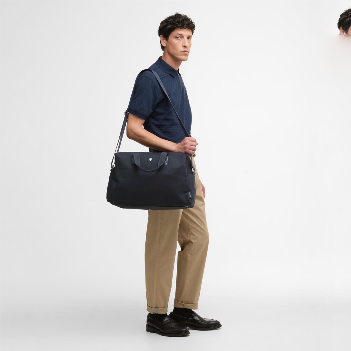 Model carries Barbour Cascade Flight Bag navy across the body with adjustable shoulder strap