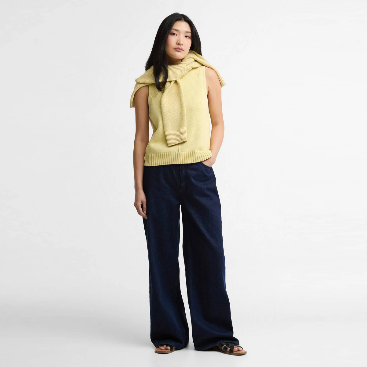 Model wearing Barbour Avon knitted vest in soured citrus with scarf draped around neck and navy wide leg trousers