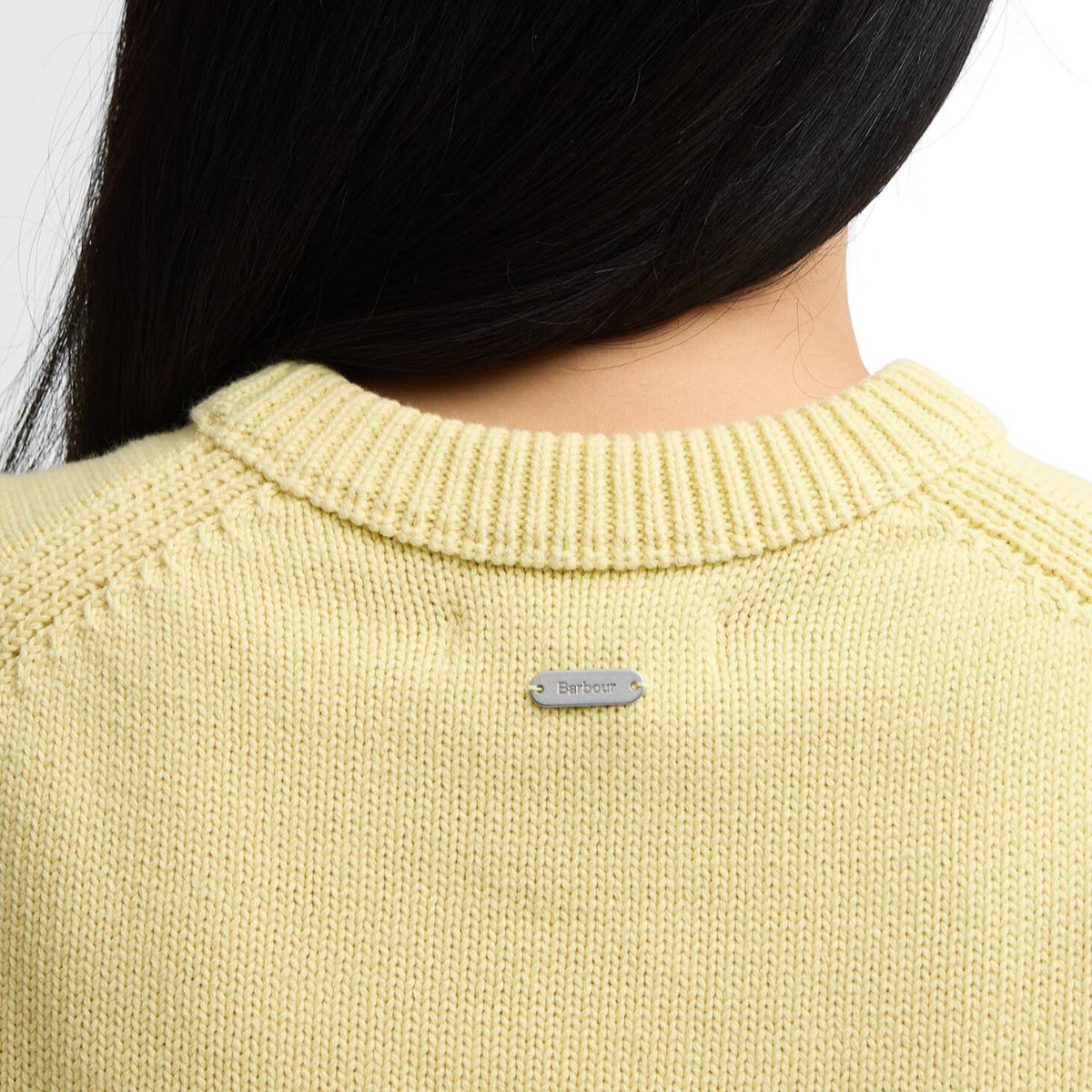 Back neck close up of pale yellow Barbour Avon knitted vest with a metal logo badge