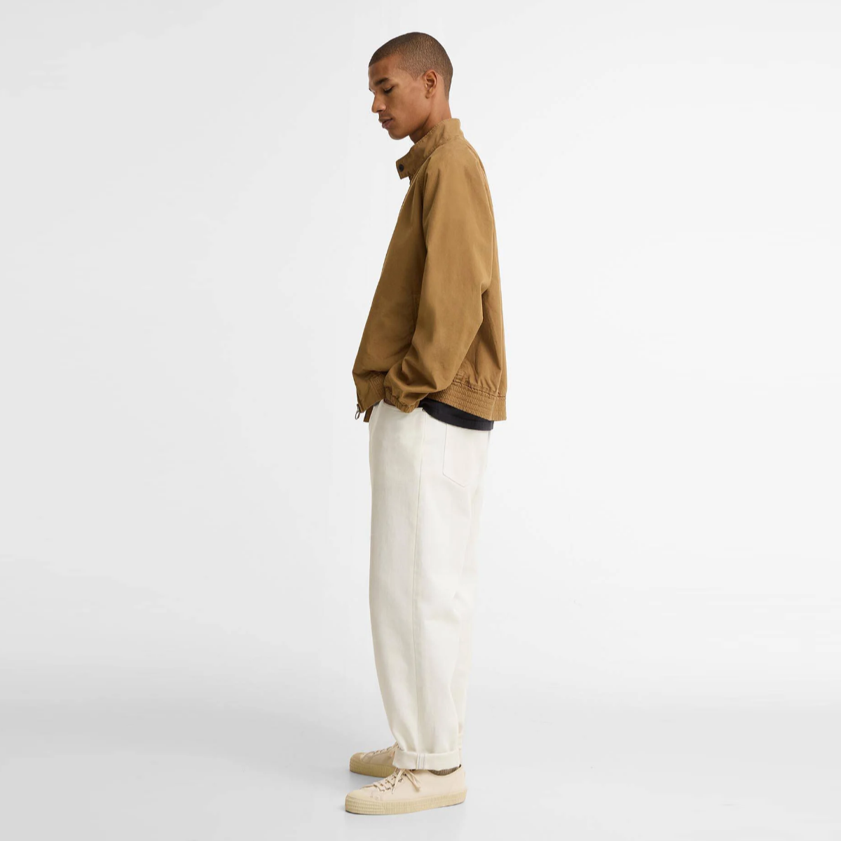 Side view of a model in camel Barbour Royston casual cotton Harrington jacket with cream trousers