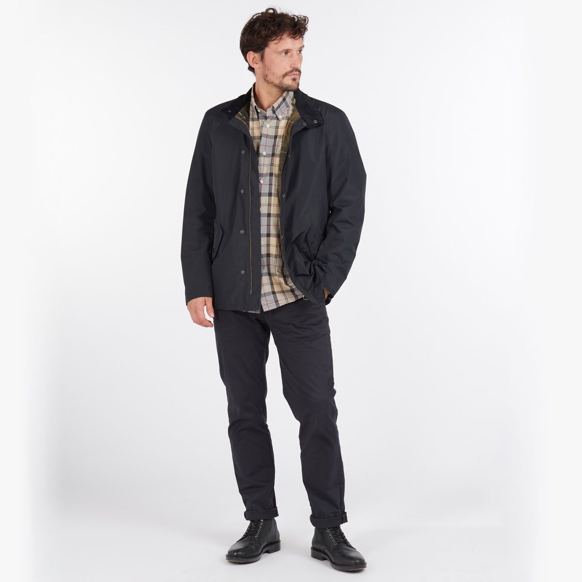 Male model in navy Barbour Spoonbill waterproof jacket worn over a plaid shirt, hands in pockets.