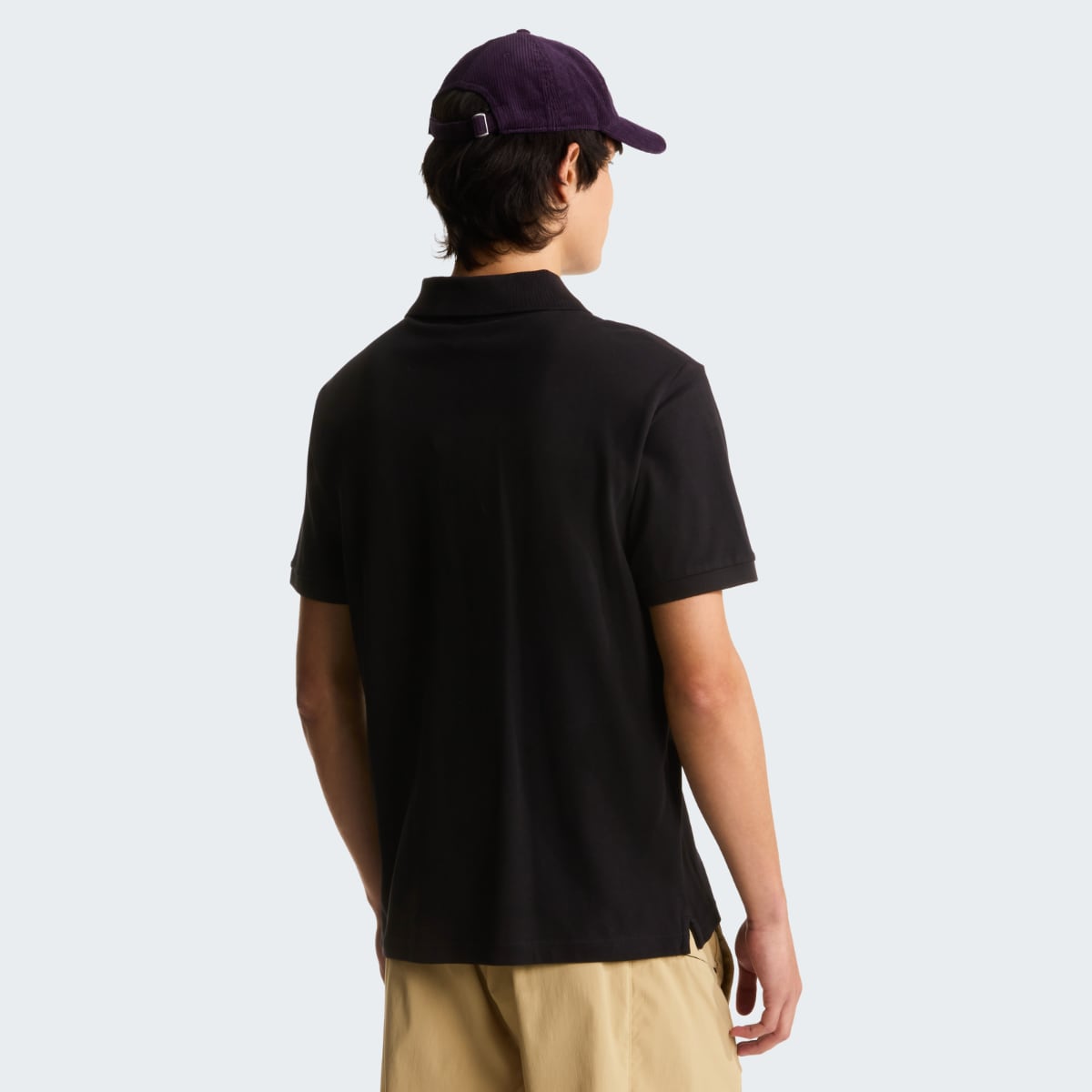 Rear view of a male model wearing a black The North Face Essential Regular Polo and a purple cap.