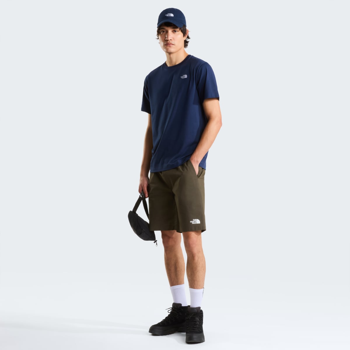 Front view of a male model wearing Summit Navy Evolution Simple Dome short sleeve t shirt with olive shorts and a small black bag.
