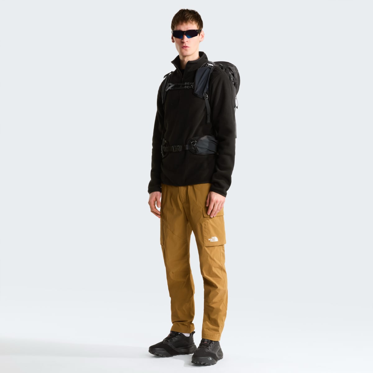 Male model wearing The North Face Glacier 1/4 Zip fleece in black with a backpack and tan cargo pants, front view