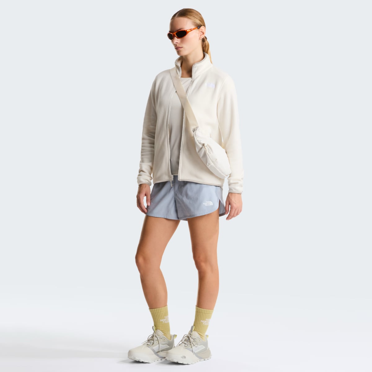 Model wearing The North Face Glacier Fleece Women's Jacket in White Dune with a beige crossbody bag and orange sunglasses