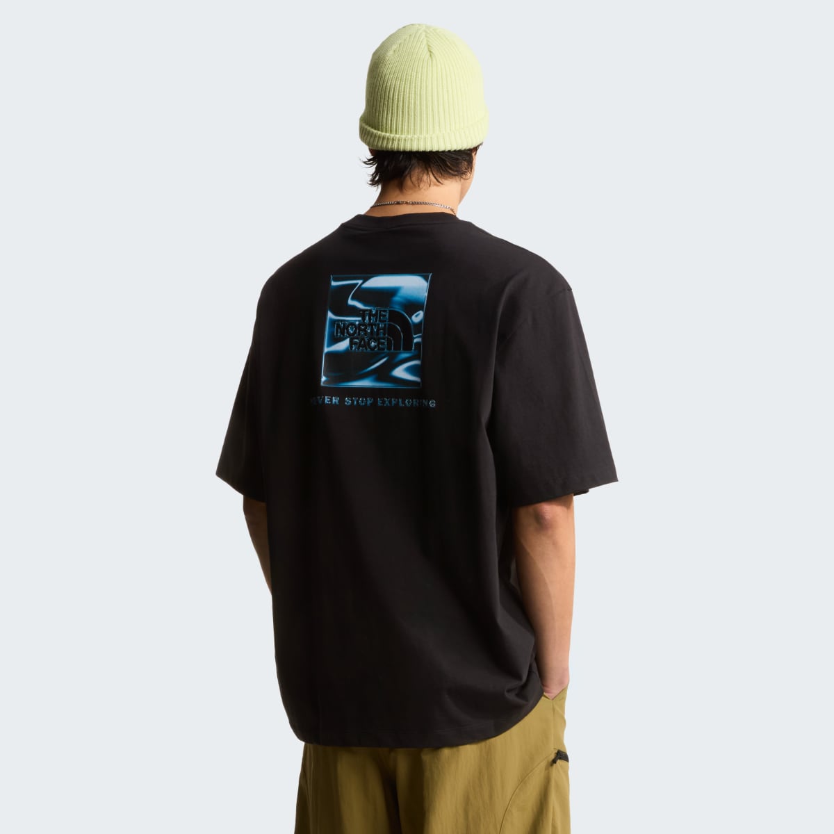 Back view of a man wearing a black The North Face Box Liquid oversize short sleeve t shirt with a blue graphic on the back