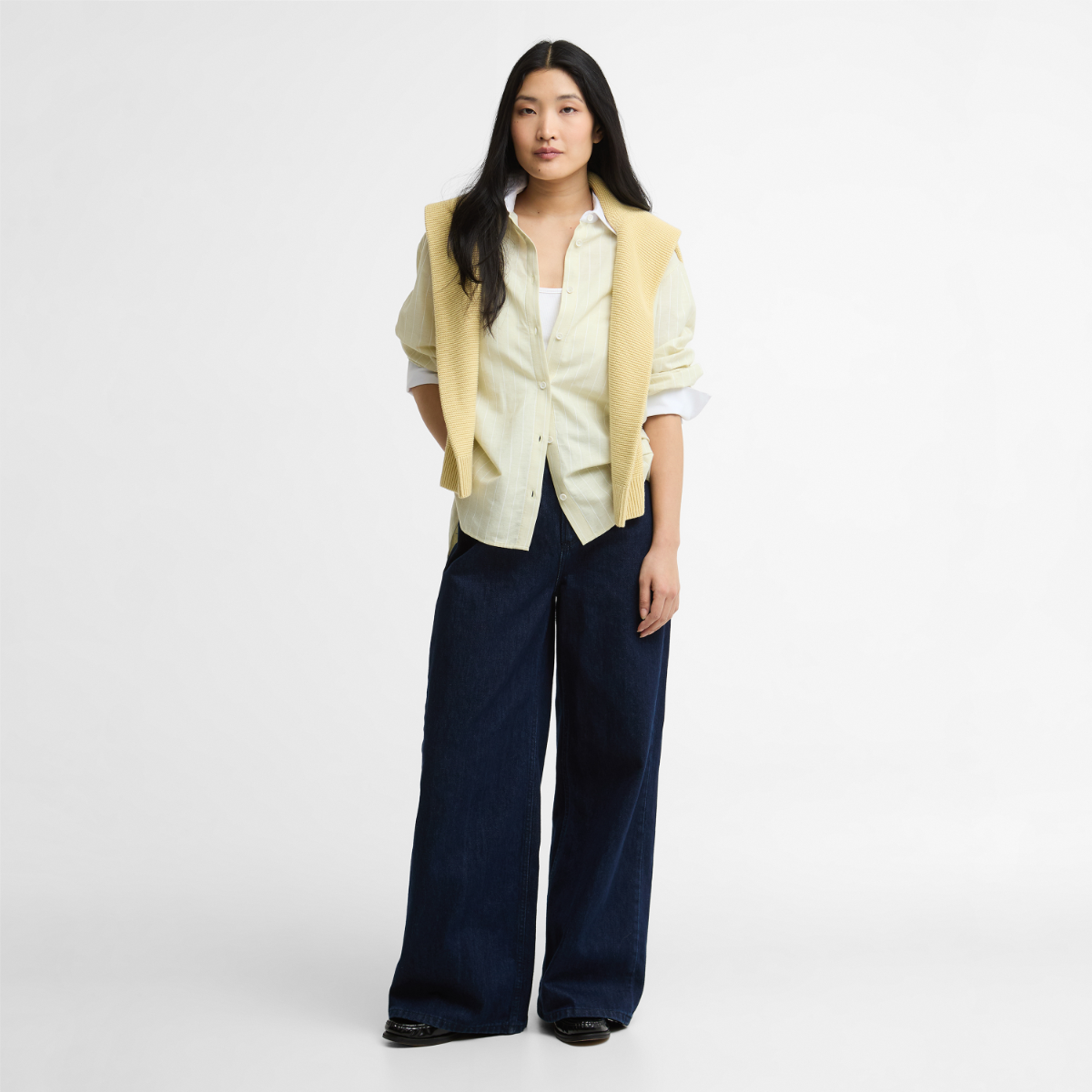 Model wearing Barbour Avon relaxed long sleeve striped shirt in soured citrus and white with a pale yellow sweater draped over shoulders
