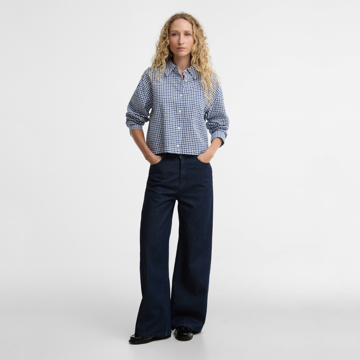 Front view of model wearing Barbour Ashwell boxy long-sleeve shirt in blue and white gingham with dark denim jeans