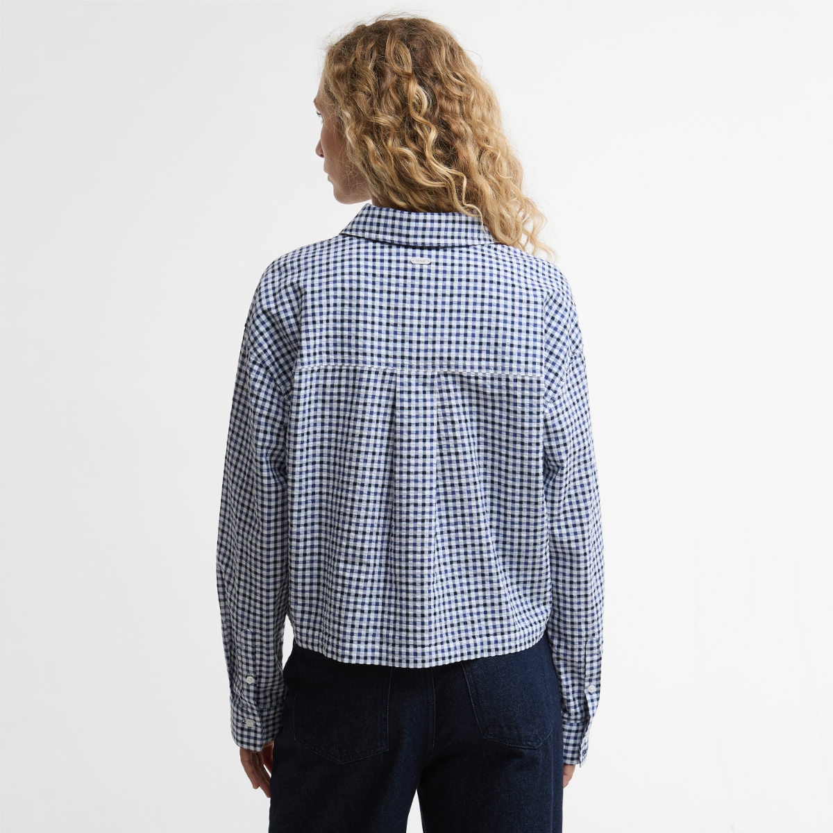 Back view of Barbour Ashwell boxy long-sleeve shirt in blue and white gingham showing yoke and relaxed fit over dark jeans