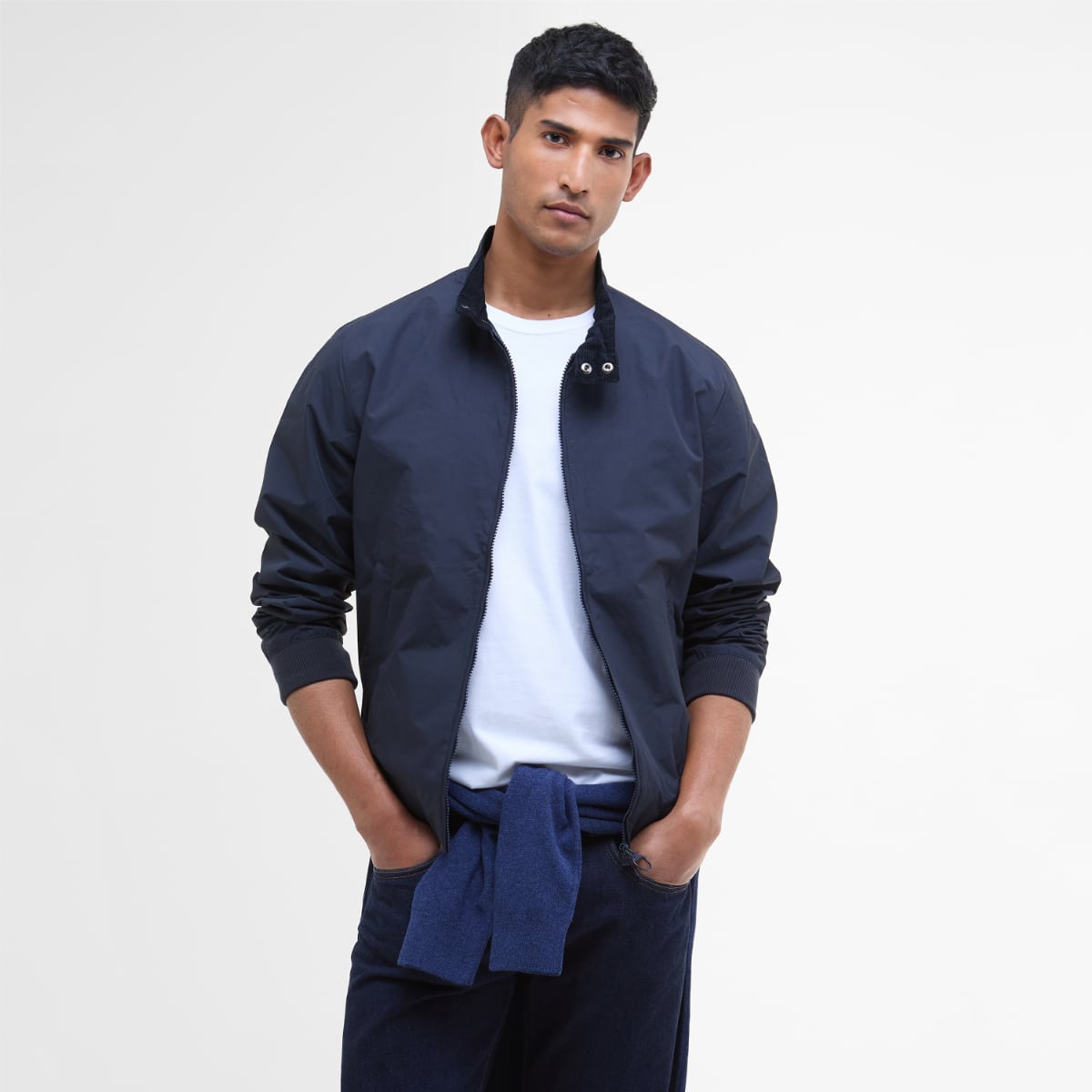 Front view of a male model in Barbour Royston navy jacket zipped up with hands in pockets and a white tee underneath