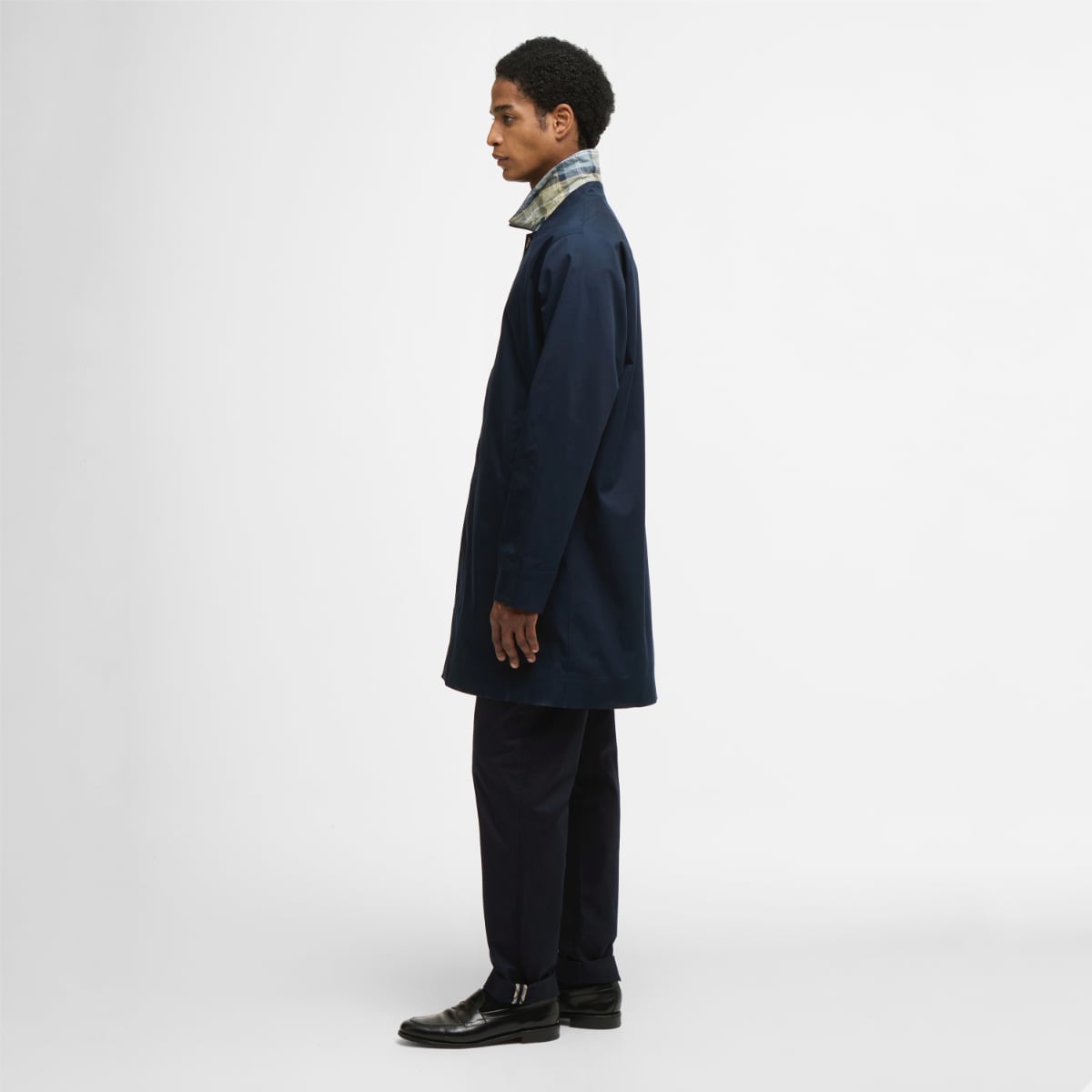 Side view of model wearing navy Barbour Rokig waterproof jacket with plaid collar peeking out