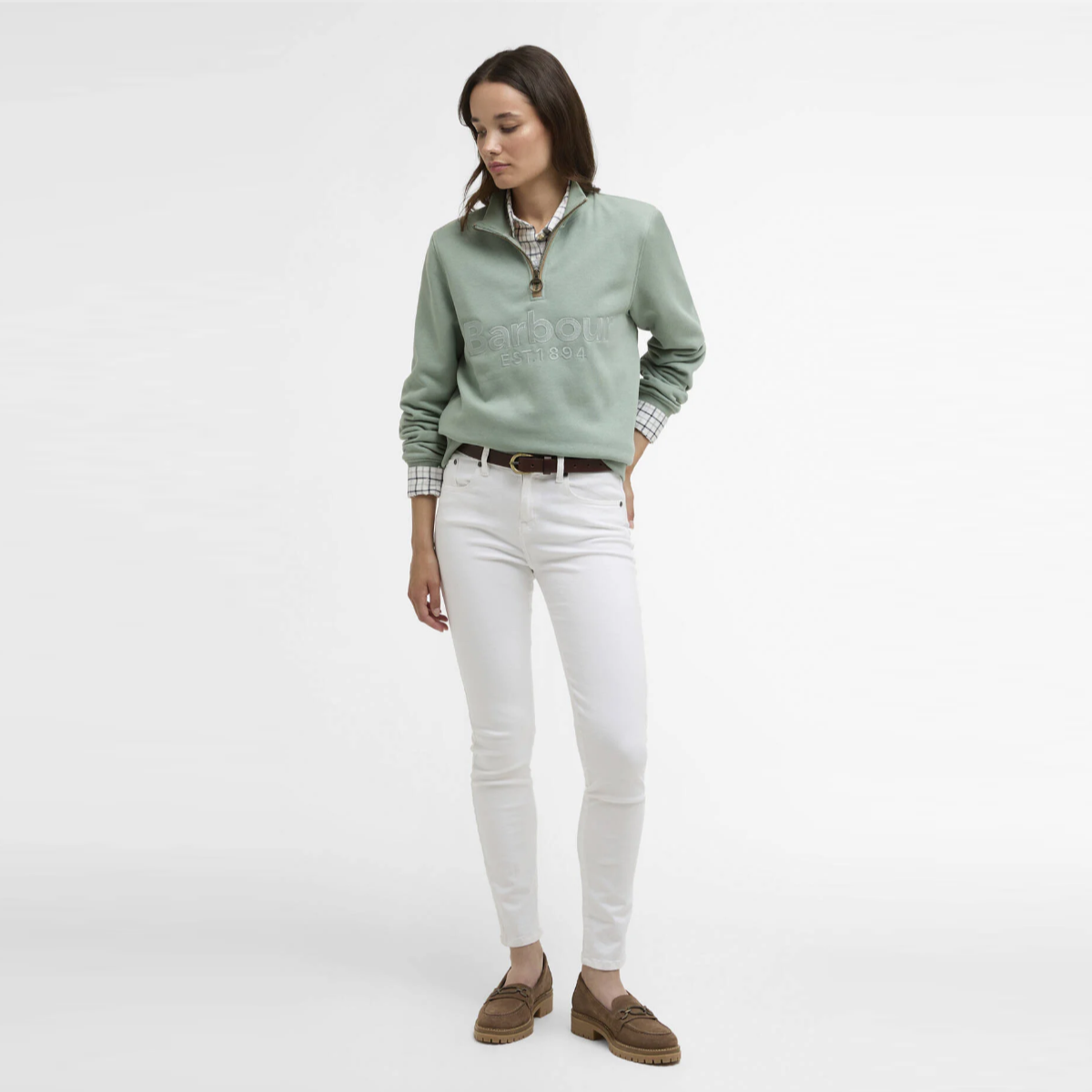 Full-length shot of a model in a Blue Sage Barbour Cynthia quarter zip jumper paired with white jeans and brown loafers.