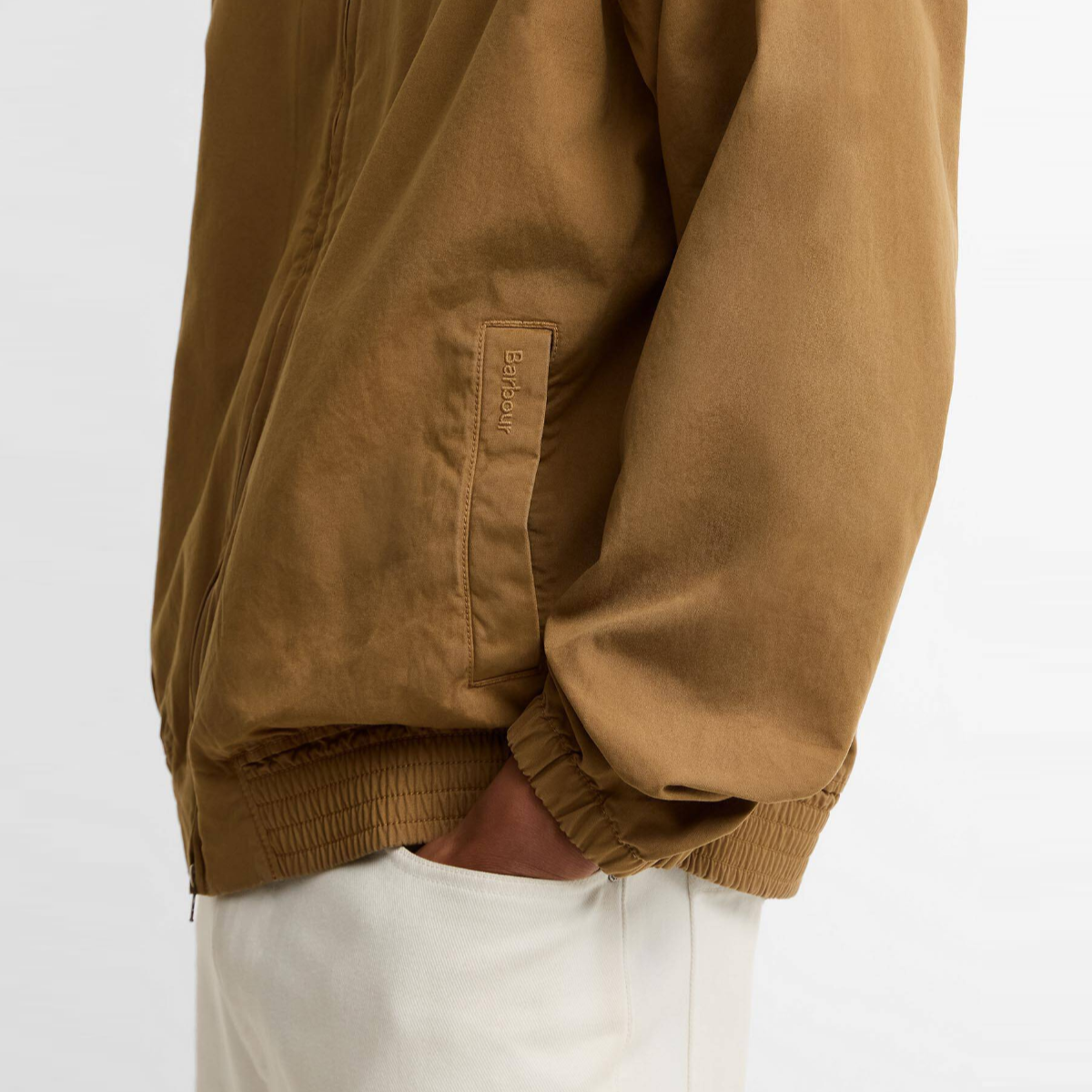 Side view of camel Harrington jacket with a visible Barbour tag on the pocket and elastic hem